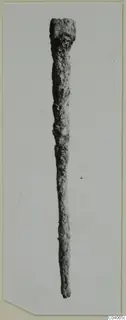 Long corroded metal object with a squared top end, shown upright from Enkomi Tomb 8