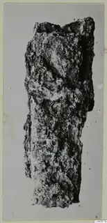 Corroded elongated metal-looking object from Enkomi Tomb 17, photographed upright against a grey background