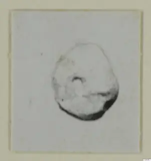 Small find from Enkomi Tomb 17, a rounded object with a hole, photographed on a plain card.