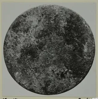 Corroded round disc photographed face-on, a find from Enkomi Tomb 17