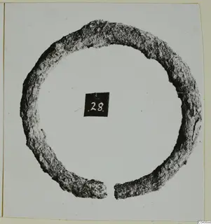Corroded metal ring with a break in its circle, from Enkomi Tomb 18, photographed with a number label