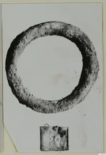 Corroded ring-shaped metal object from Enkomi Tomb 18, photographed face-on with a small number label below