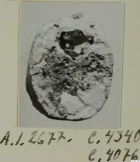 Oval stone seal or gem with a worn, pitted surface, photographed and mounted on a cream card