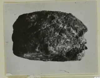 Dark, rough stone object, possibly a seal, shown on a grey card mount