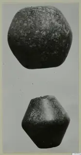 Two dark stone objects, one rounded and one faceted, photographed one above the other against a grey background.