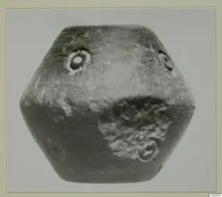 Hexagonal stone object with small circular perforations, photographed against a pale background.