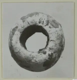 Ring-shaped bead, pale grey with dark patches and a large central hole, photographed face-on