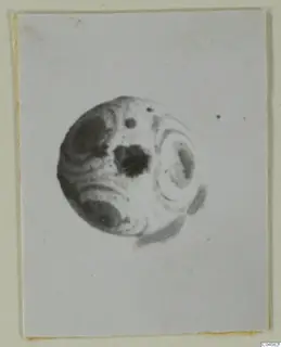 Round bead with dark blotches and curved bands of tone, shown on a mounted photograph card