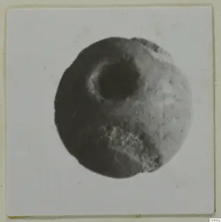 Round stone object with a large central hole, shown face-on in a photograph mounted on card