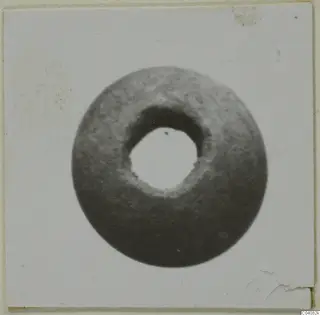 Round stone object with a large central hole, seen face-on against a pale background.