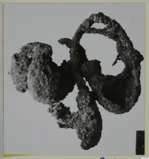 Corroded silver find: a lumpy, encrusted mass of metal with loops and open gaps, photographed on a pale background.