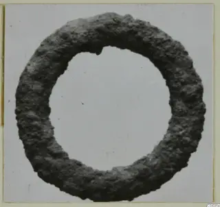 Corroded metal ring with a pitted, dark surface, photographed face-on against a pale background.