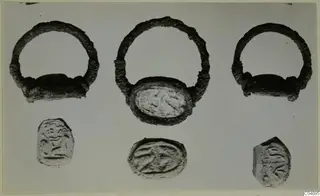 Three silver rings with oval bezels above three engraved glyptic objects, photographed on a grey background