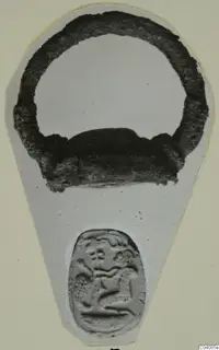 Dark metal ring above a pale seal impression showing a small figure, photographed on a grey card, from Marion.