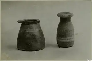 Two stone vases with flared rims, one squat and one tall, photographed side by side on a plain grey backdrop.