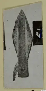 Bronze weapon head, leaf-shaped with a central ridge and a broken lower end, photographed on a mounted card