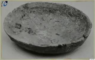 Shallow bowl with a rounded body and uneven rim, photographed at an angle on a pale background