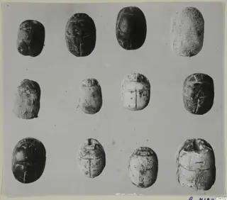 Several scarab-shaped stones with incised patterns, from Arsos, arranged in rows on a grey background.