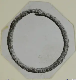 Corroded ring-shaped metal object from Arsos, shown on an octagonal card mount