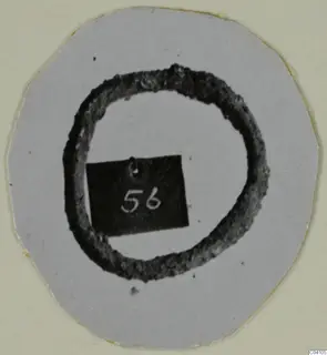 Corroded dark metal ring on a grey card, with a small black number label