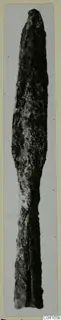 Long, corroded metal blade from Ayios Iakovos Tomb 14, shown upright against a pale backdrop