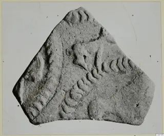 Irregular fragment with raised arc-shaped relief decoration, photographed against a plain grey background