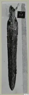 Corroded bronze blade from Ayios Iakovos Tomb 14, shown with a number label