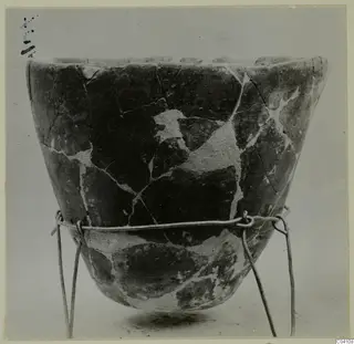 Pieced-together pottery vessel with a wide mouth, shown on a wire stand.