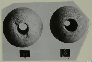 Two round stone objects with central holes, photographed on grey card, from Nitovikla T.I