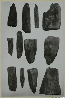About a dozen dark, weathered fragments arranged in three rows on a pale ground, from Amathus