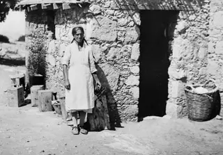 Eleni standing in front of a stone building with a dark doorway at Vouni