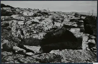 Rocky stone remains at Vouni Temple of Athena, with a wooden fence on the right and hills in the distance.