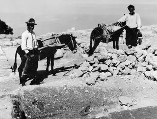 Two men with laden donkeys beside a heap of rubble at the palace at Vouni