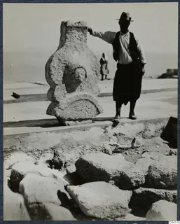 Man in a hat resting his hand on a weathered carved stone figure at the palace at Vouni.