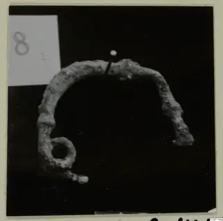 Corroded bronze arched object with a round loop at one end, from Amathus tombs, shown against a black background