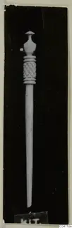 Bone pin with a carved lattice band below an ornate head, shown against a dark background