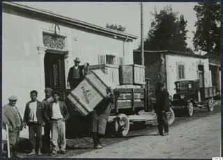 Men loading wooden crates onto a lorry in a street in Nicosia, one man carrying a crate on his shoulder.