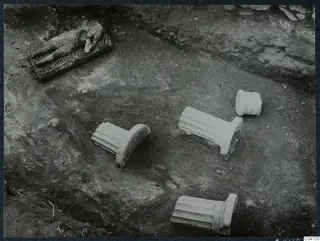 Excavated floor of a room with fluted stone column pieces and a carved stone block lying in place