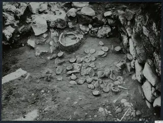 Finds in situ on the floor of an excavated area at Cholades, Soli, with a stone wall behind them.