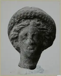 Terracotta figurine head with a wavy headdress and a short neck stub, photographed against a plain light background