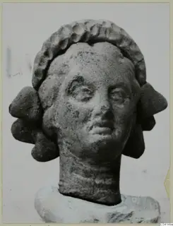 Terracotta female head with a curled hair band and side locks, shown against a plain background, from Soli.