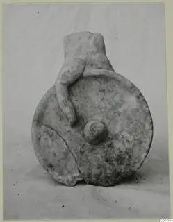 Carved stone object: a round flat disc with a cylindrical neck, with a small figure clinging to its side.