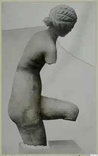 Marble sculpture of a female figure with hair in a bun, arms broken off, one leg bent up, on a block base