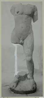 Stone statue of a nude male figure, headless and armless, standing on a circular base, from Soli
