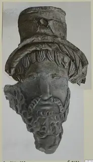Terracotta head fragment with a tall cylindrical headdress and a curled beard, photographed on a pale card mount