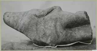 Marble sculpture fragment, a weathered pale stone piece lying on its side on a grey surface