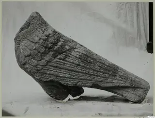 Stone fragment from Soli, tapering, with overlapping scale-like carving on one side and horizontal ridges on the other.