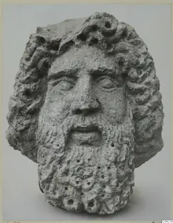 Stone head of a bearded figure with curling hair and a pitted surface, from Soli