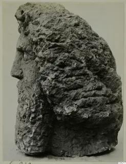 Carved stone head in left profile, with rough, weathered hair or beard in heavy ridged masses