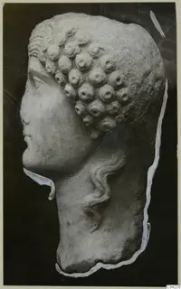 Marble head sculpture in profile facing left, with rows of rounded curls and a wavy lock falling down the neck